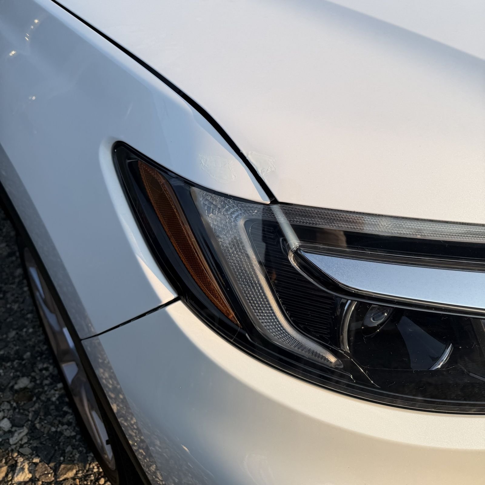 Clear headlight and freshly repaired hood edge on a white vehicle